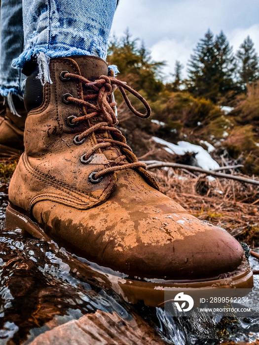 One wet cowboy boot stepping on the water in the mountains at winter season.