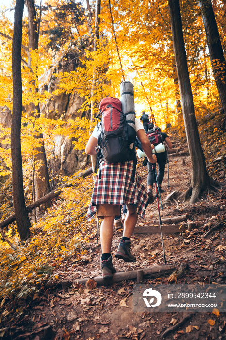 Group of friends with backpacks trekking together and climbing in forest