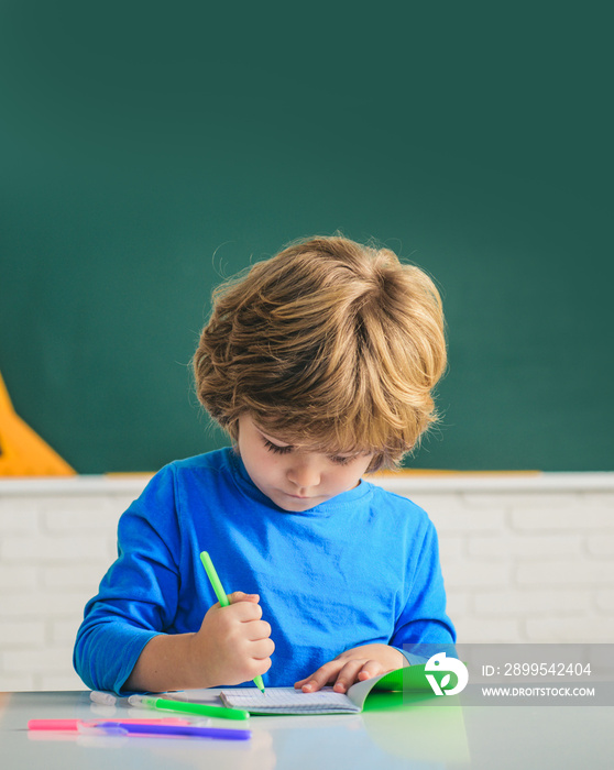 Happy cute industrious child is sitting at a desk indoors. Cute pupil with funny face schooling work. Kids gets ready for school.