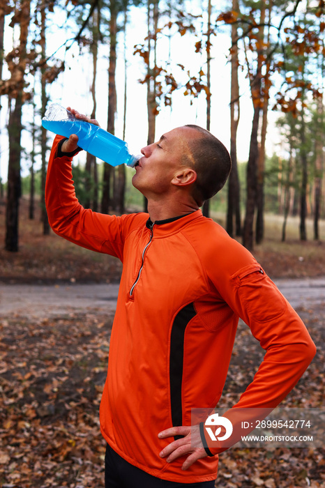 Male runner, athlete, drinks isotonic, energy drink after a hard workout in the open air. Sports nutrition