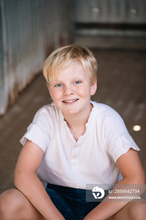 Cute blonde pre-teen boy with relaxed pose in rustic outdoor setting