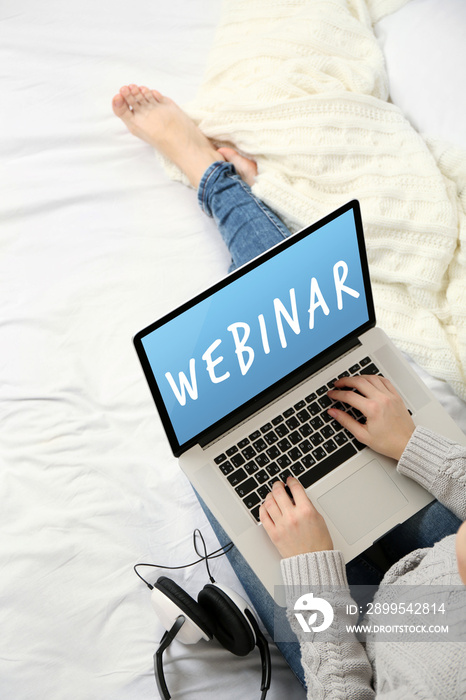 Woman using laptop on her bed. Webinar concept