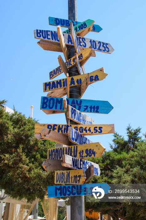 Signpost giving directions and distances to multiples cities all around the world on the beach of Cala Llonga in the southeast of Ibiza in the Balearic Islands, Spain