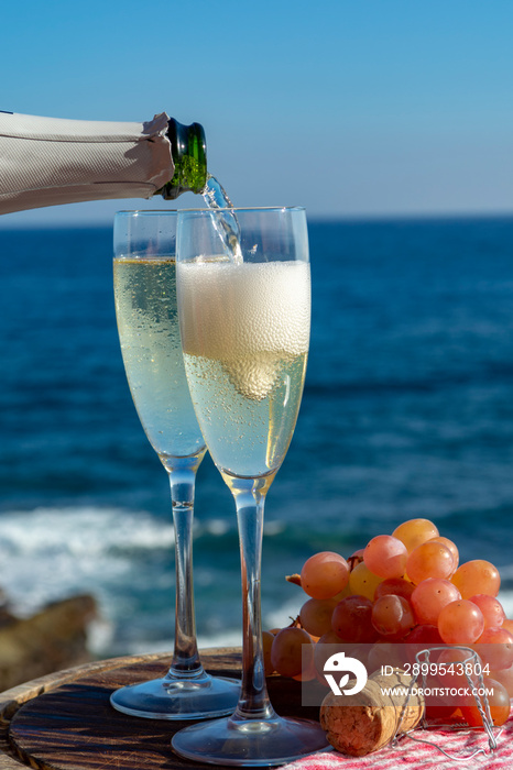 Waiter pouring Champagne, prosecco or cava in two glasses on outside terrace with sea view