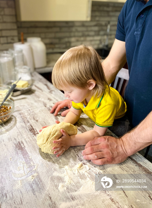 A fair-skinned little child with his father / grandfather prepares sweet rolls filled with cottage cheese and raisins in the kitchen at home. A step-by-step cooking process.Defocus light background.