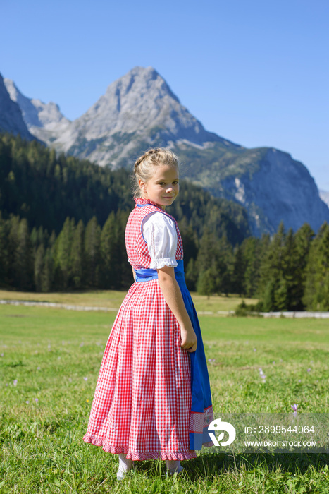 Adorable bavarian girl in a beautiful mountain landscape.Smiling little girl wearing a traditional Bavarian dress dirndl.