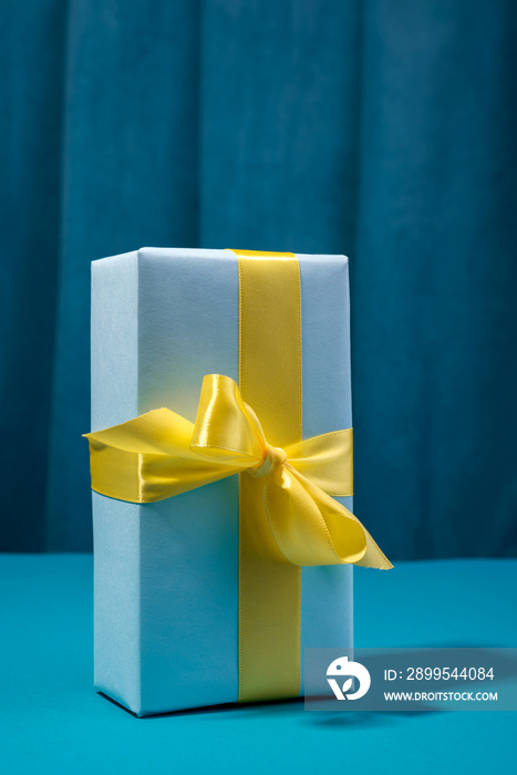 Gift box with Yellow bow against bold blue background and curtain.