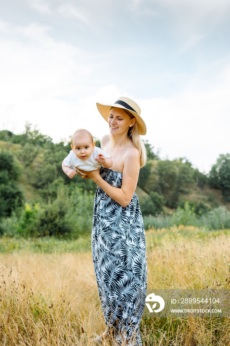 Happy mother holding infant baby outdoors wearing sun hat at summer day