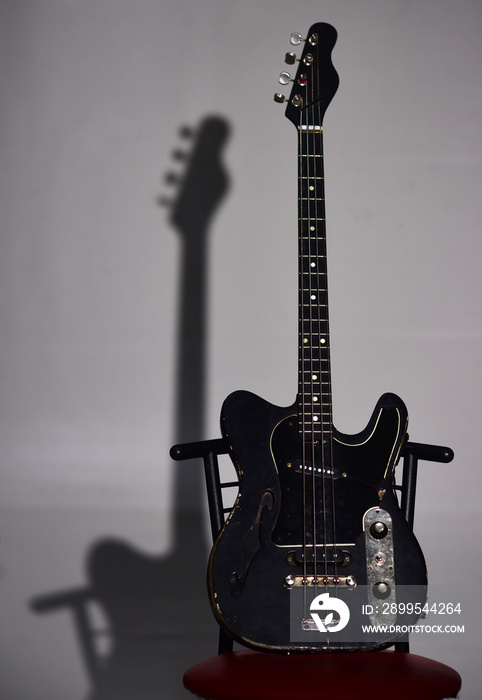 Electric guitar stands on dark red chair. Musical instrument