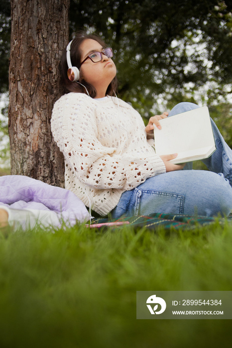 Happy woman with Down syndrome reading and listening to music in the park