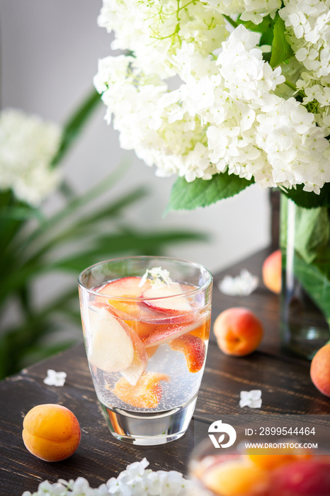 Refreshing drink with apricots and peaches, cold sparkling water with fruits, a vase of flowers viburnum opulus Roseum and a glass with a drink