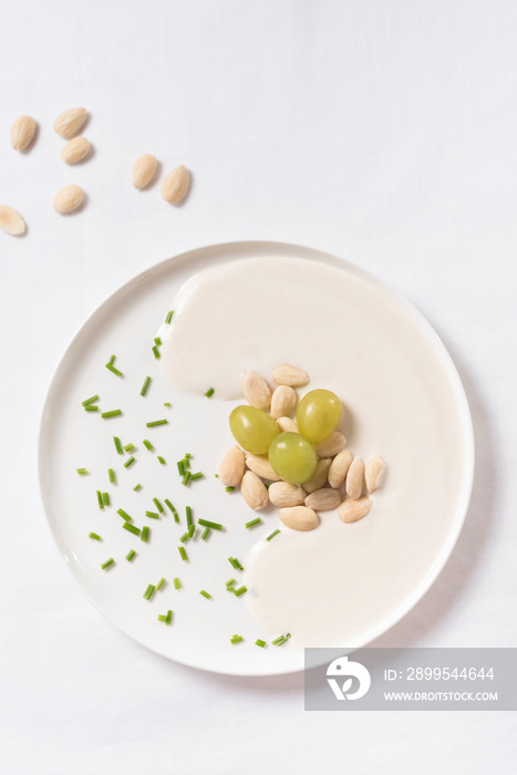 Crema de almendras, sopa fría española. Ajo blanco de Málaga con almendras y uvas en un recipiente blanco sobre una mesa blanca. Vista superior