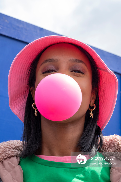 Portrait of young woman in bucket hat blowing bubble gum