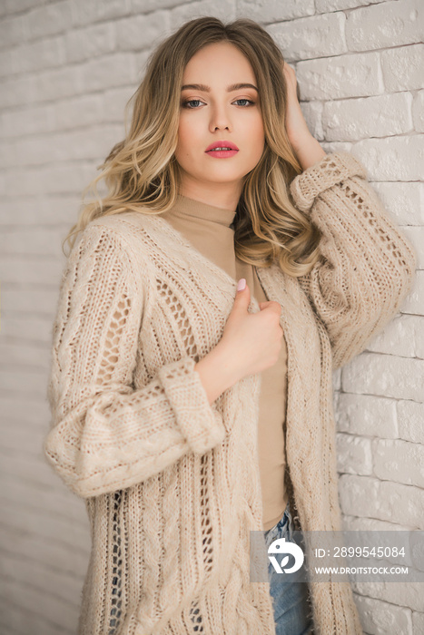 Young blonde curly woman in beige knitted cardigan portrait