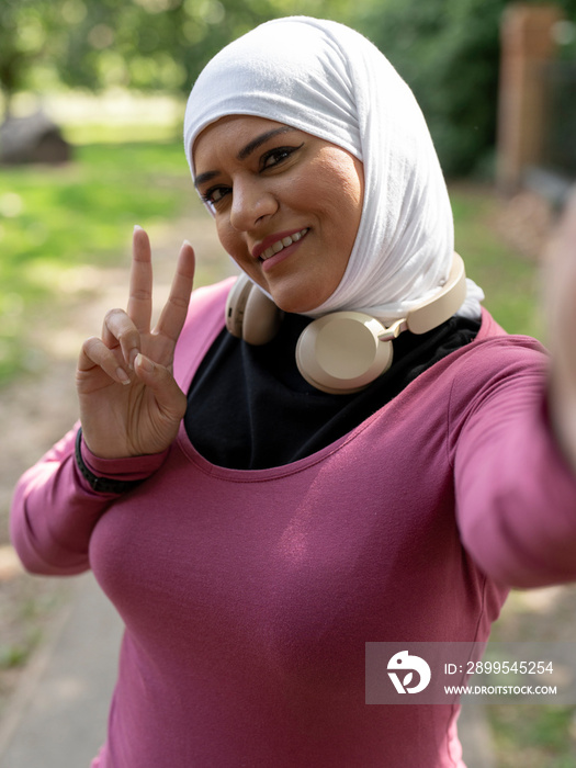 UK,Sutton,Portrait of smiling woman in headscarf showing peace sign