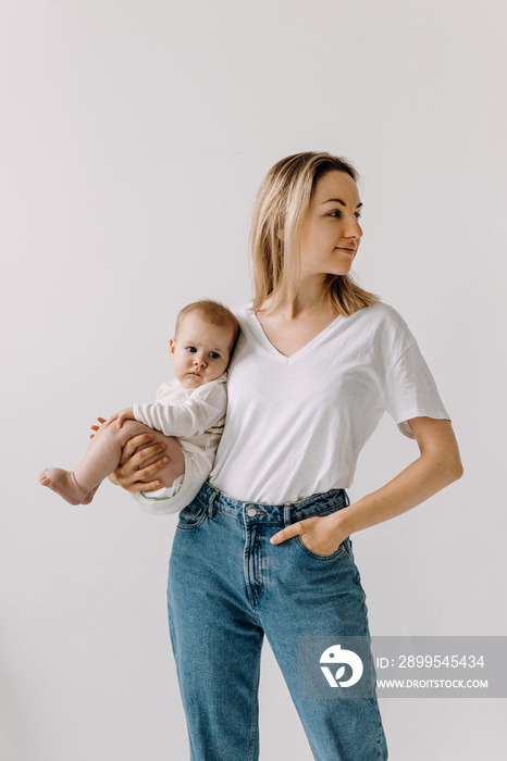 Mother holding her baby with one arm, on white wall background, looking to side.