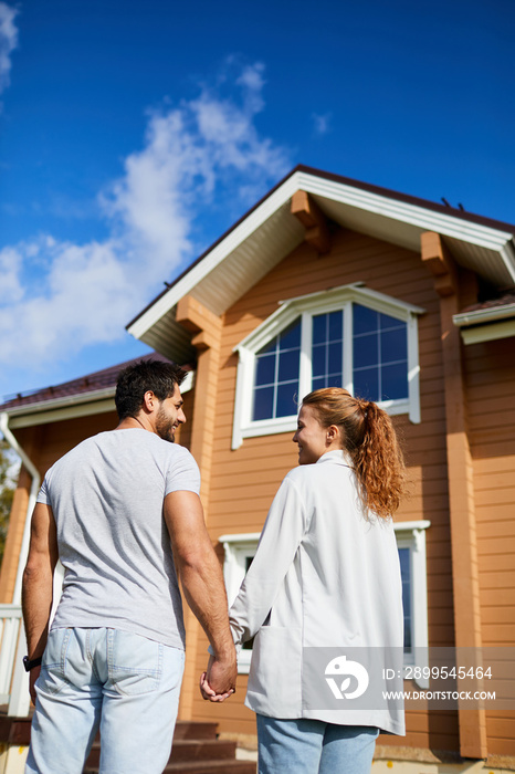 Back view of new owners of house standing in front of it anad looking at one another