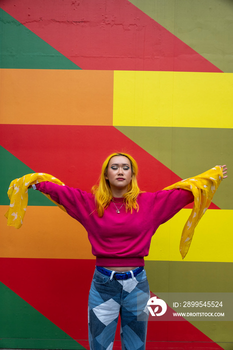 Young woman with yellow hair standing against colorful wall