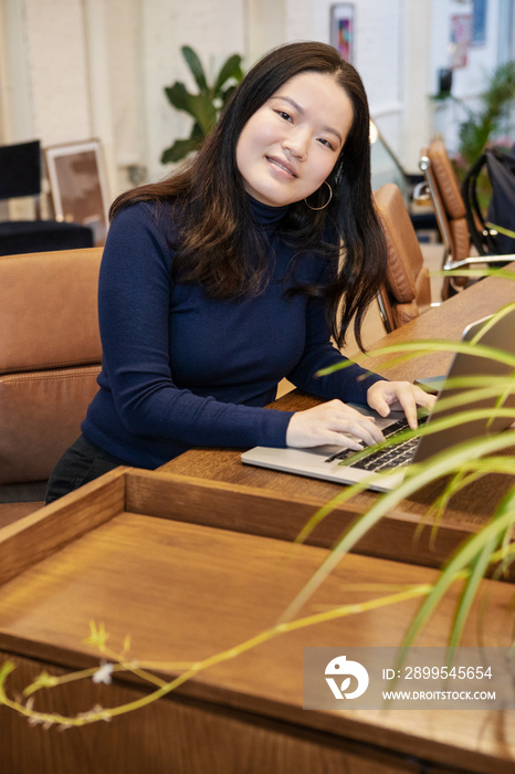 Portrait of smiling woman using laptop at desk