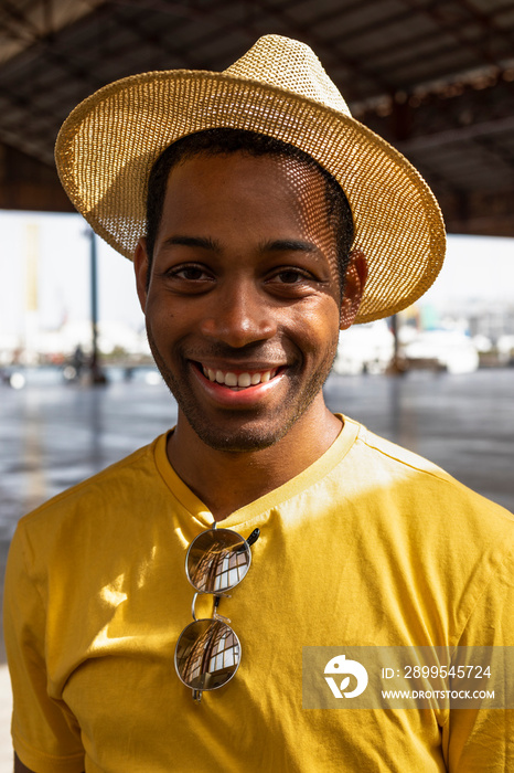 Young black man in yellow T-shirt with straw hat and mirrored glasses smiling in camara.