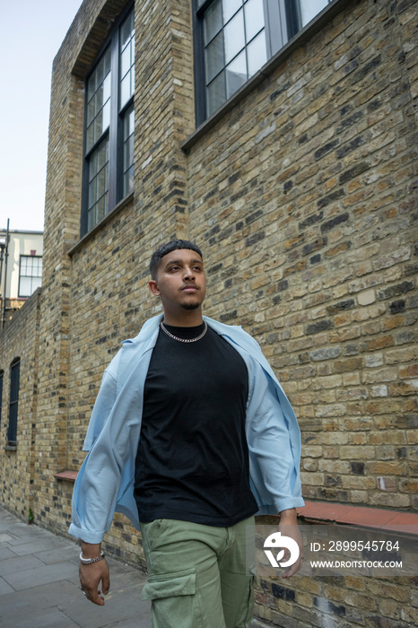 Man wearing unbuttoned shirt and cargo pants walking along brick wall