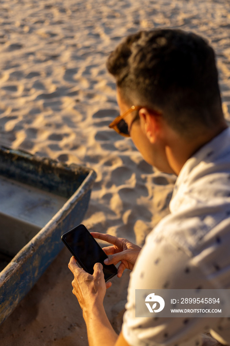 Man sitting at beach and using smart phone