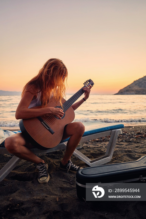 Silhouette of a blonde female playing acoustic guitar on the beach at sunset