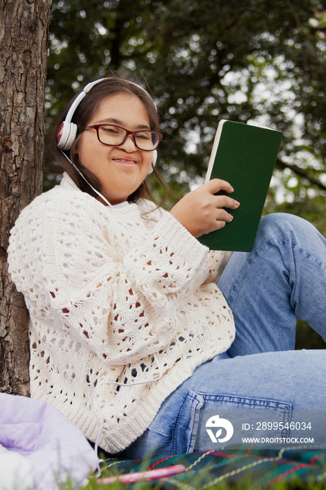 Happy woman with Down syndrome reading and listening to music in the park