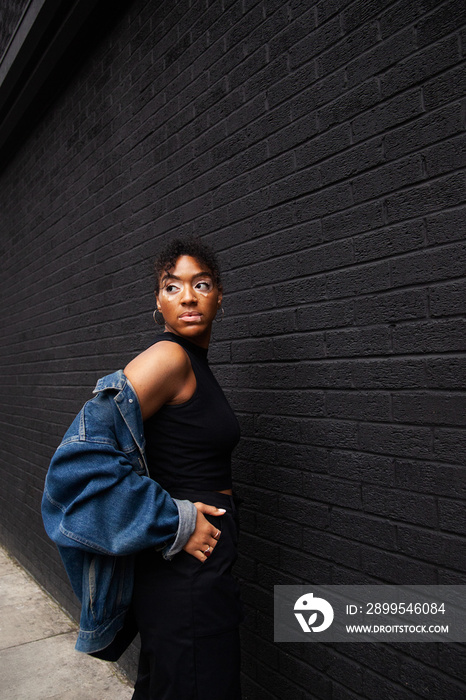 Mid-sized woman of mixed race in jeans jacket posing in front of black wall