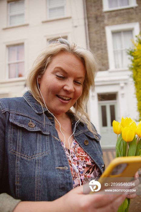 Curvy woman in her 40s smiling at her phone outdoors wearing earphones