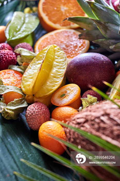 Summer exotic fruits - carambola, pineapple, coconut, mango, kiwi, halves of orange on a green tropical leaf.