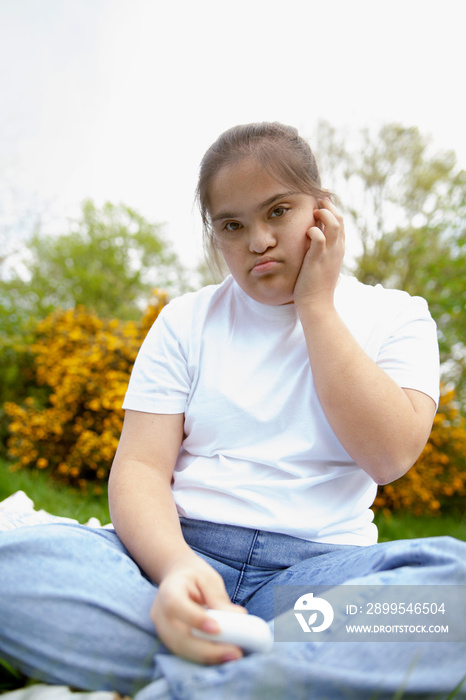 Young curvy woman with Down Syndrome sitting in a park with earbuds