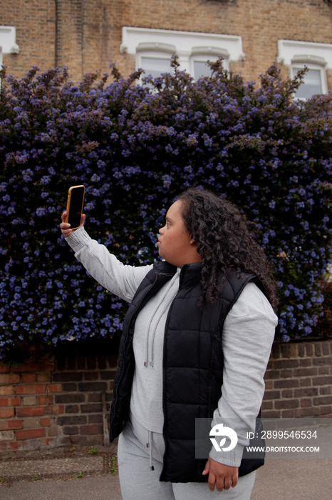 Young plus-sized women with Down Syndrome taking selfie in front of flowers