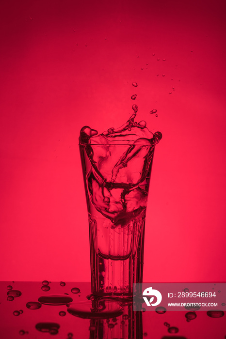 Splash of water in a glass on a red background. Unusual sculptures