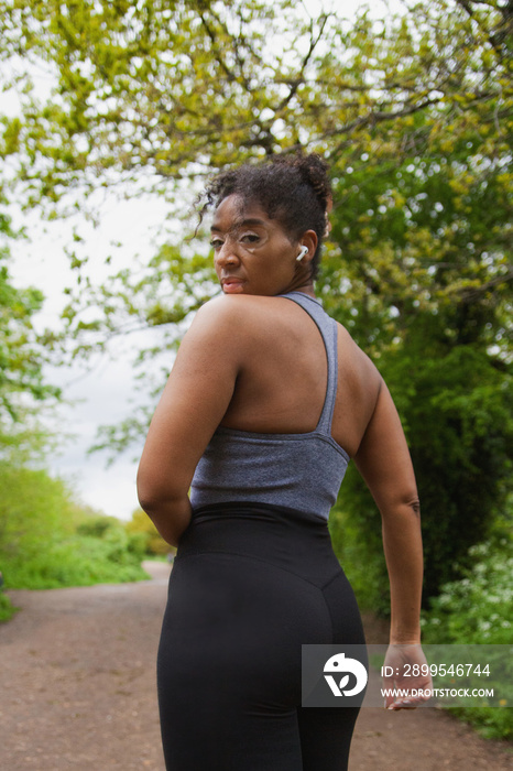 Young curvy woman with vitiligo working out in the park  with earbuds and looking fierce