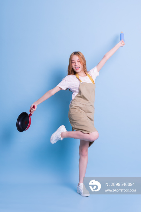 Image of young Asian woman holding pan on blue background