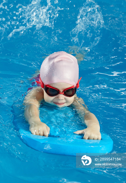 Little girl learning to swim in indoor pool with pool board