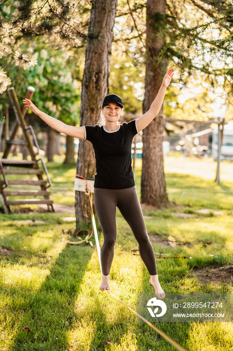 Slacklining is a practice in balance that typically uses nylon or polyester webbing. Girl walking on a slackline in a park during a sunset. Slack line