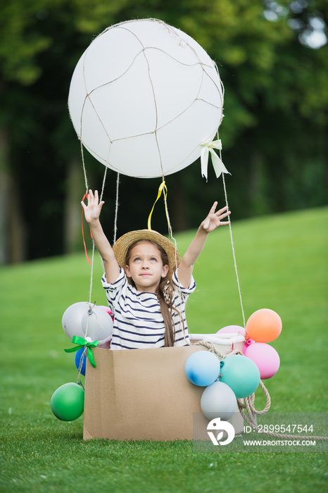 Adorable little girl in straw hat sitting in toy hot air balloon while playing in park