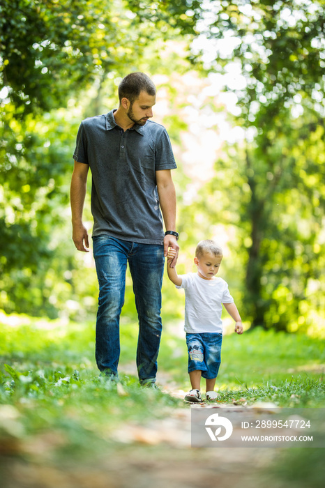 Happy young father holding his little son by hand and walking on the park