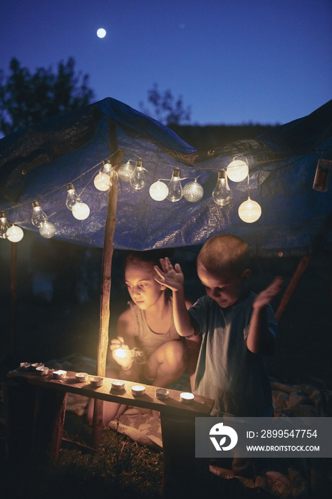 Kids making a small tent with candles and lampions in the backyard.