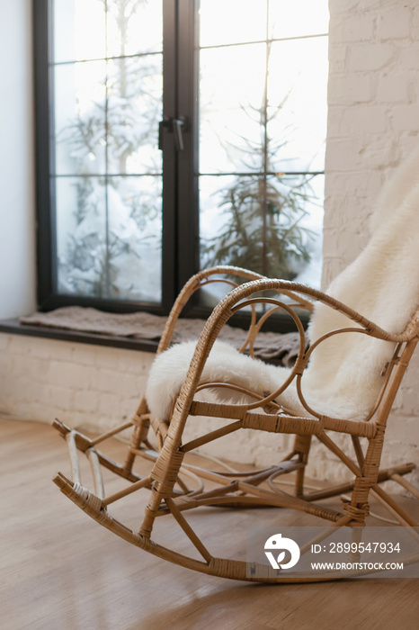 wicker rocking armchair at home with big panoramic french windows and cozy lighting at chalet home or lodge. Cosy home cottagecore aesthetic interior in winter season