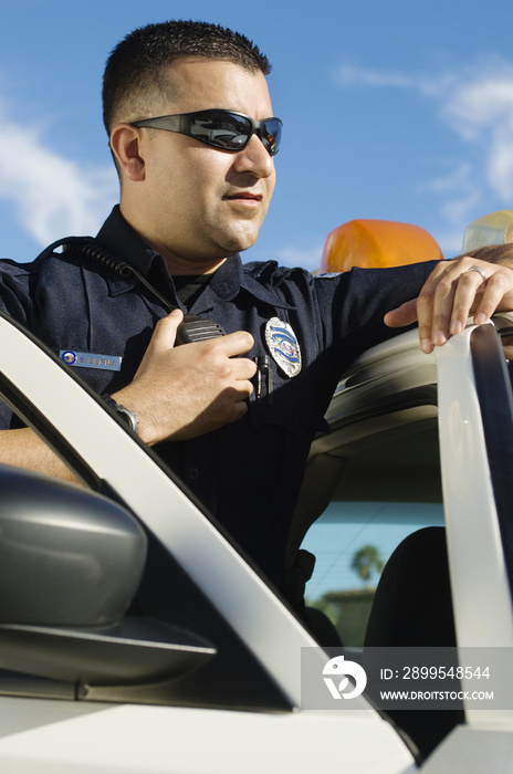 Male police officer using two-way radio while leaning on car