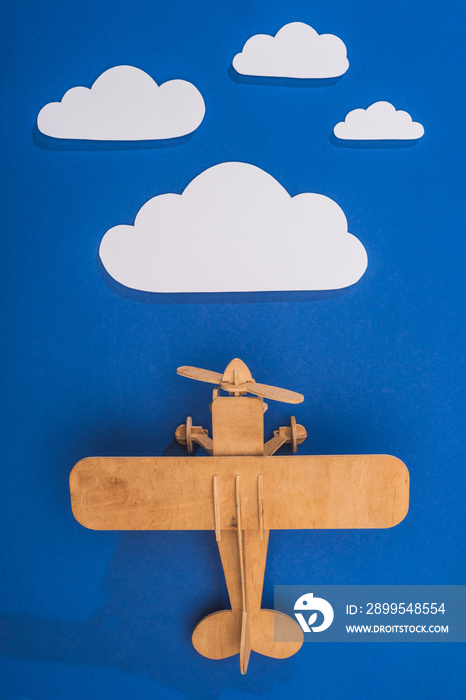 top view of wooden toy plane in blue sky with paper cut white clouds