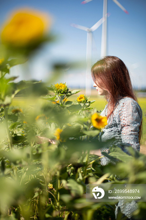 White young girl with dark hair standing with sky behind in sunflower field