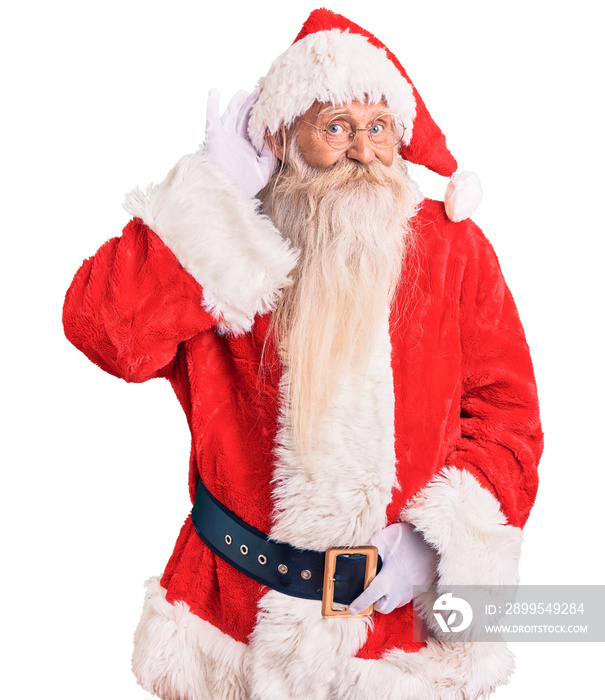 Old senior man with grey hair and long beard wearing traditional santa claus costume smiling with hand over ear listening an hearing to rumor or gossip. deafness concept.