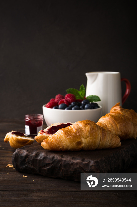 Delicious breakfast with fresh croissants and ripe berries on old wooden background. Healthy food concept with copy space. Dark photo.