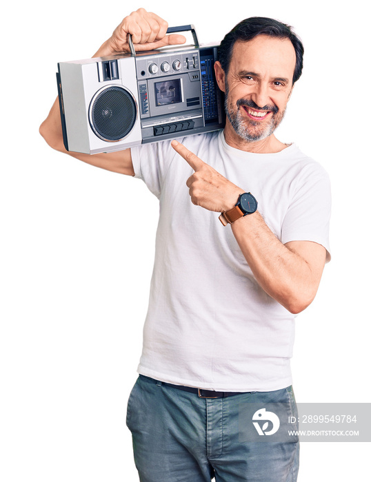 Middle age handsome man listening to music using vintage boombox smiling happy pointing with hand and finger
