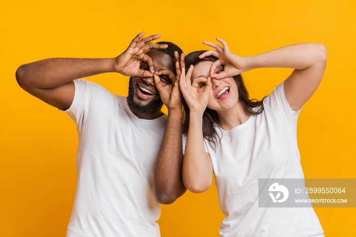 Cheerful interracial couple making funny glasses with fingers, fooling together