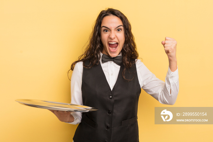 young pretty hispanic woman shouting aggressively with an angry expression. waiter and tray concept